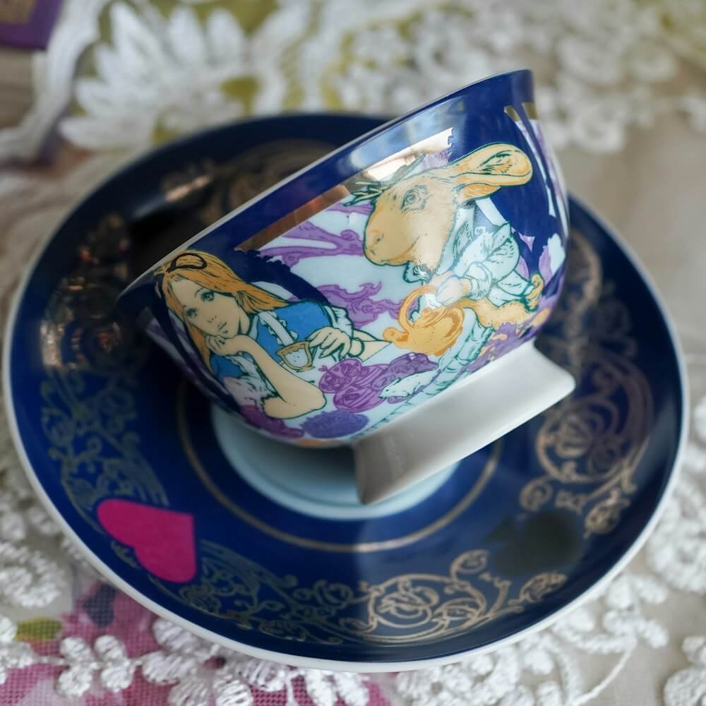 Alice in Wonderland Tea Cup and saucer with Alice, the Hatter, and the March Hare sitting at a tea party surrounded by mushrooms and whimsical designs.