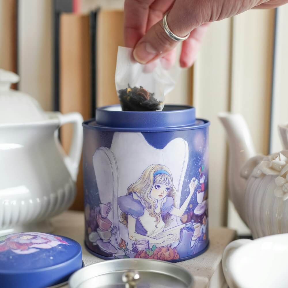 Round metal Alice in Wonderland Tea Tin with Alice, Mad Hatter, and Rabbit sitting at a table for tea time. 