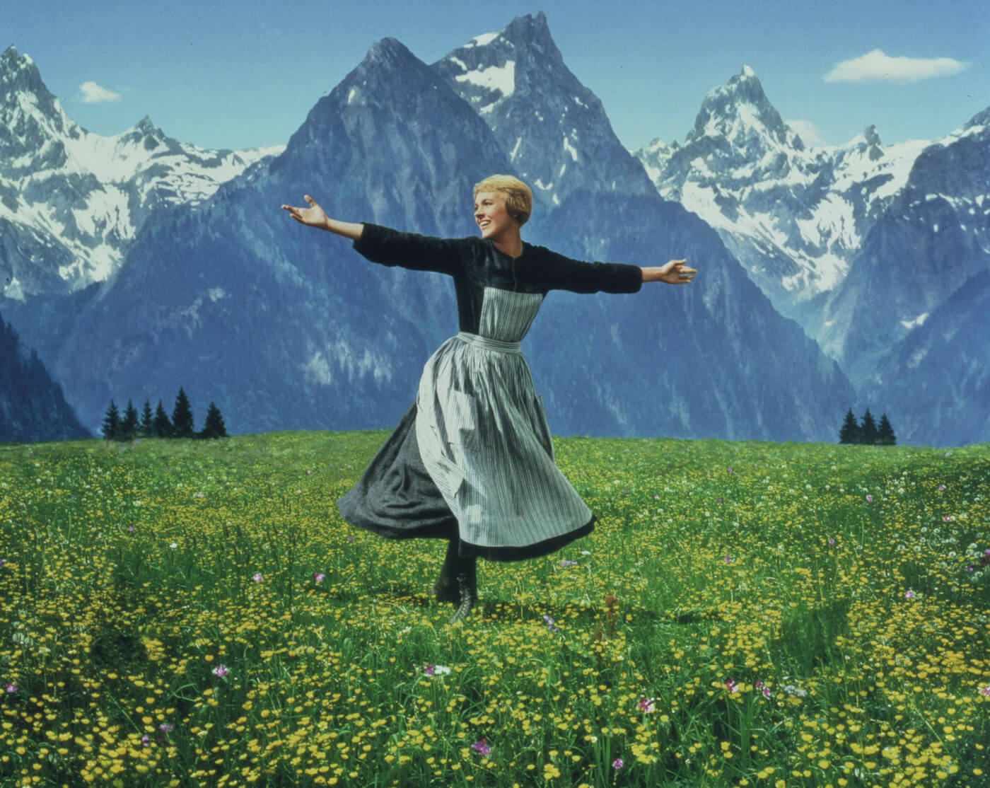 Maria from Sound of Music dancing on green grass with mountains behind her