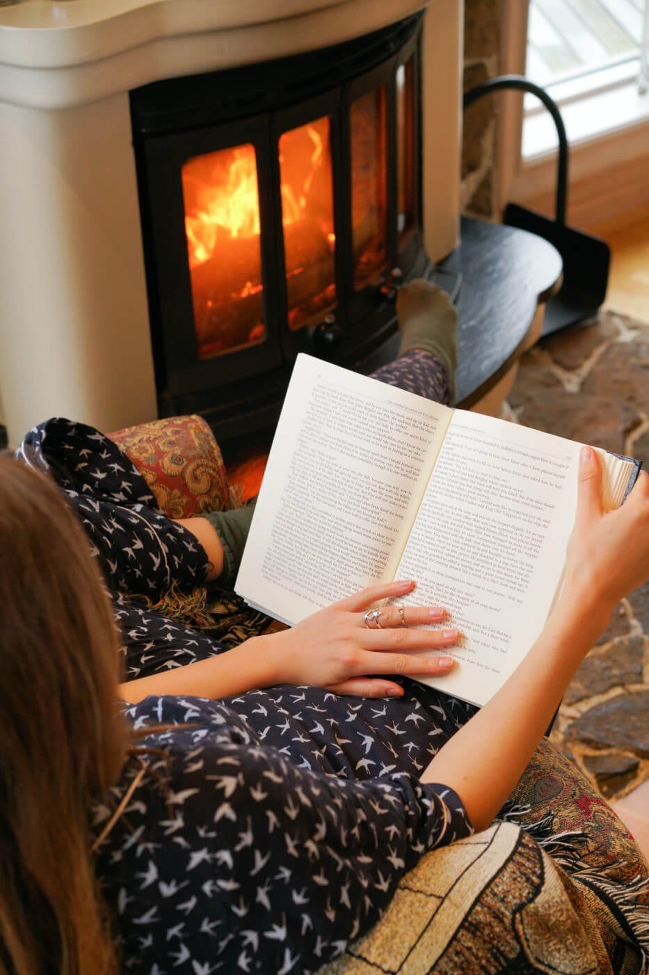 person in pajamas reading in front of fireplace