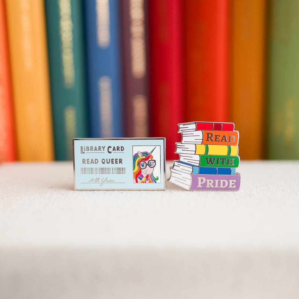 Pride Pin Set #1: a library card enamel pin that says "read queer" and a colorful stack of books that says "read with pride"