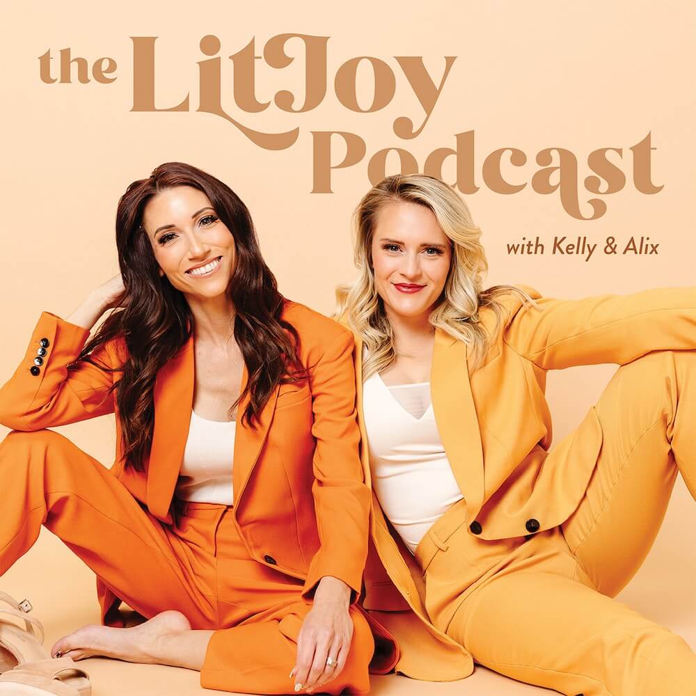 Kelly sitting on left in an orange power suit and shoes kicked off; Alix sitting on right in a yellow power suit supported by Kelly 