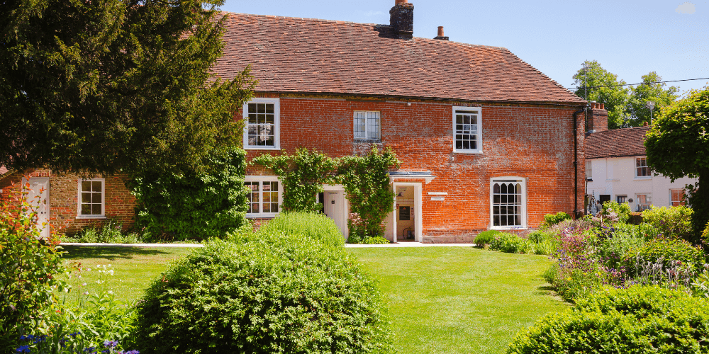 an old red house resembling jane austen period surrounded by bushes and trees