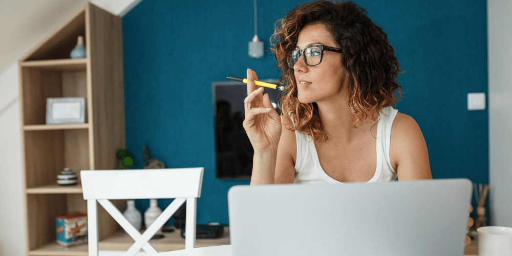 girl with glasses sitting at a laptop and holding a pencil