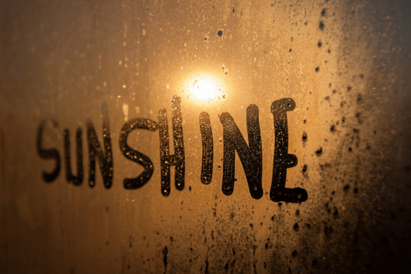 The words "sunshine" drawn in a fogged up window with rain outside