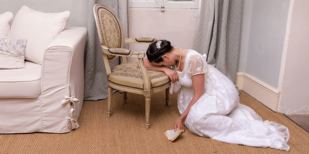 regency era woman sits on the floor and cries onto a chair