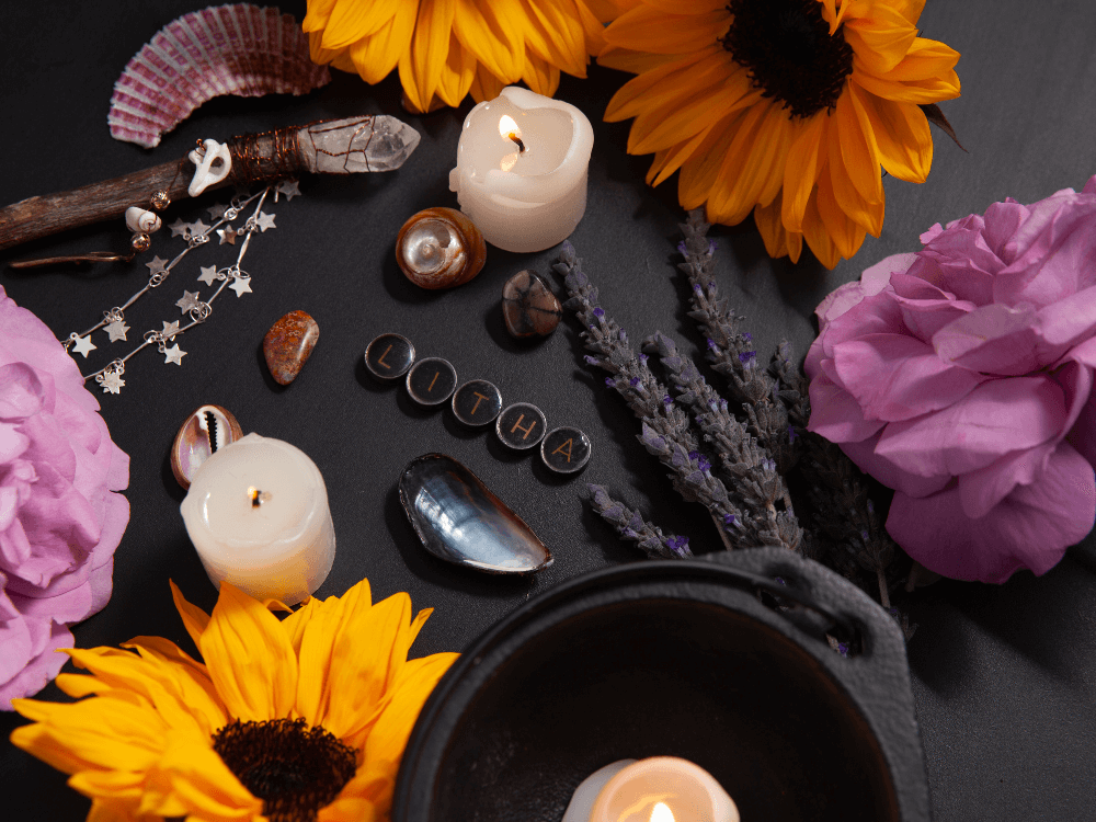 Symbols of Litha (Summer Solstice) showing roses, sunflowers, a candle, and stones