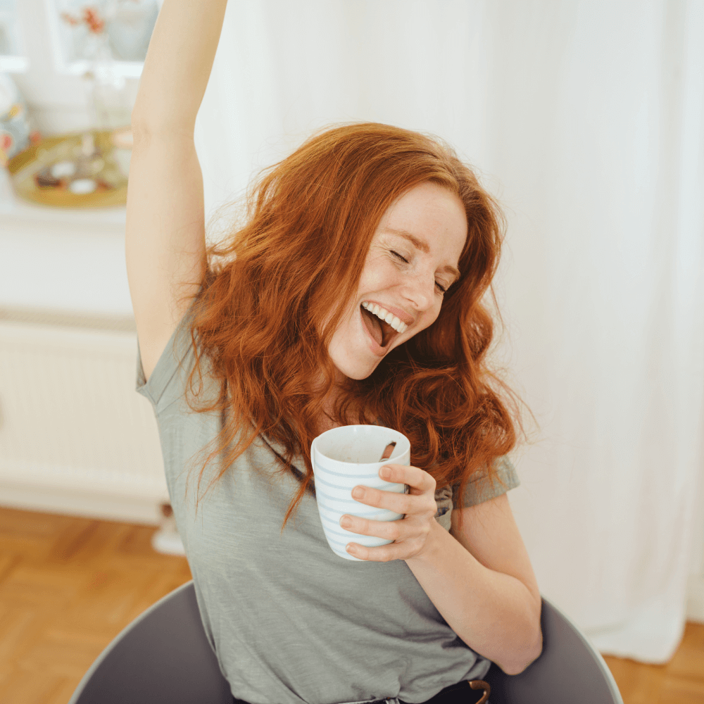 woman with red hair holding a cup of coffee and cheering